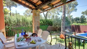 An outdoor dining area with a table set for two, surrounded by chairs, with a pool and greenery in the background. - Níspero - Two Bedroom Villa, Sleeps 4 (Begur)