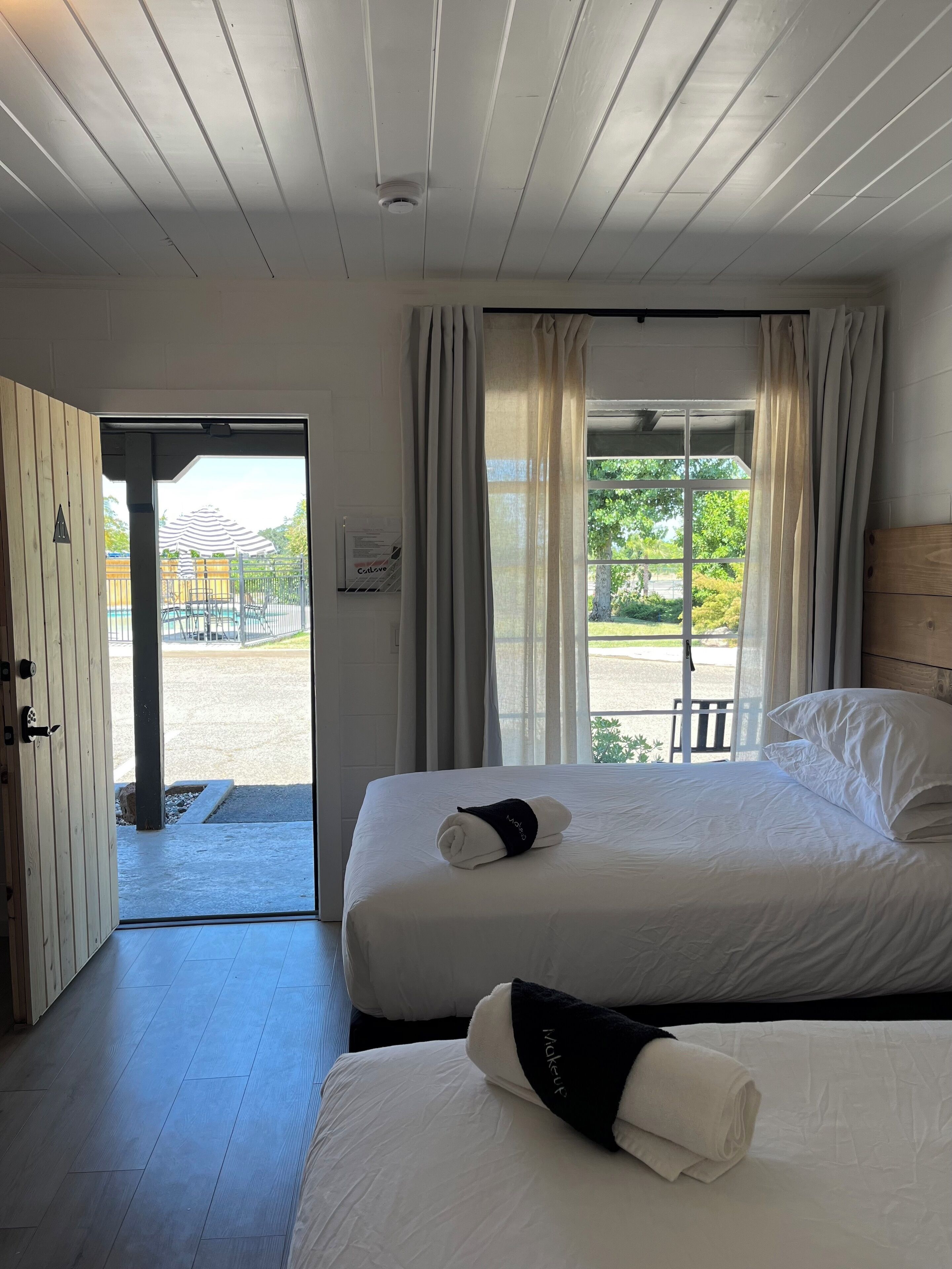Quarto de hotel com duas camas, teto de madeira, vista para área externa e porta que dá para o exterior.