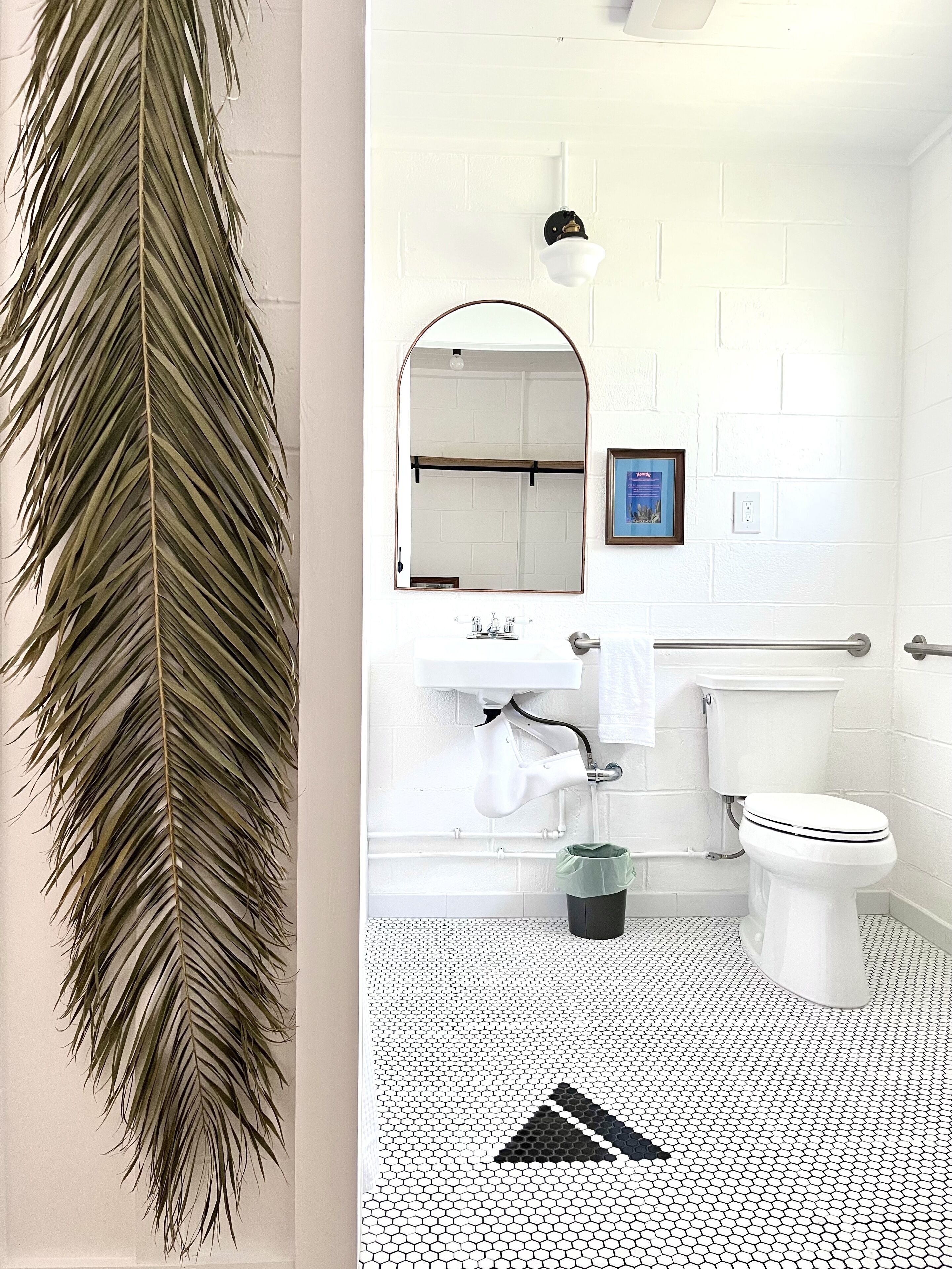 A bathroom with a white tiled floor, a toilet, a sink with a mirror above it, and a framed picture on the wall.