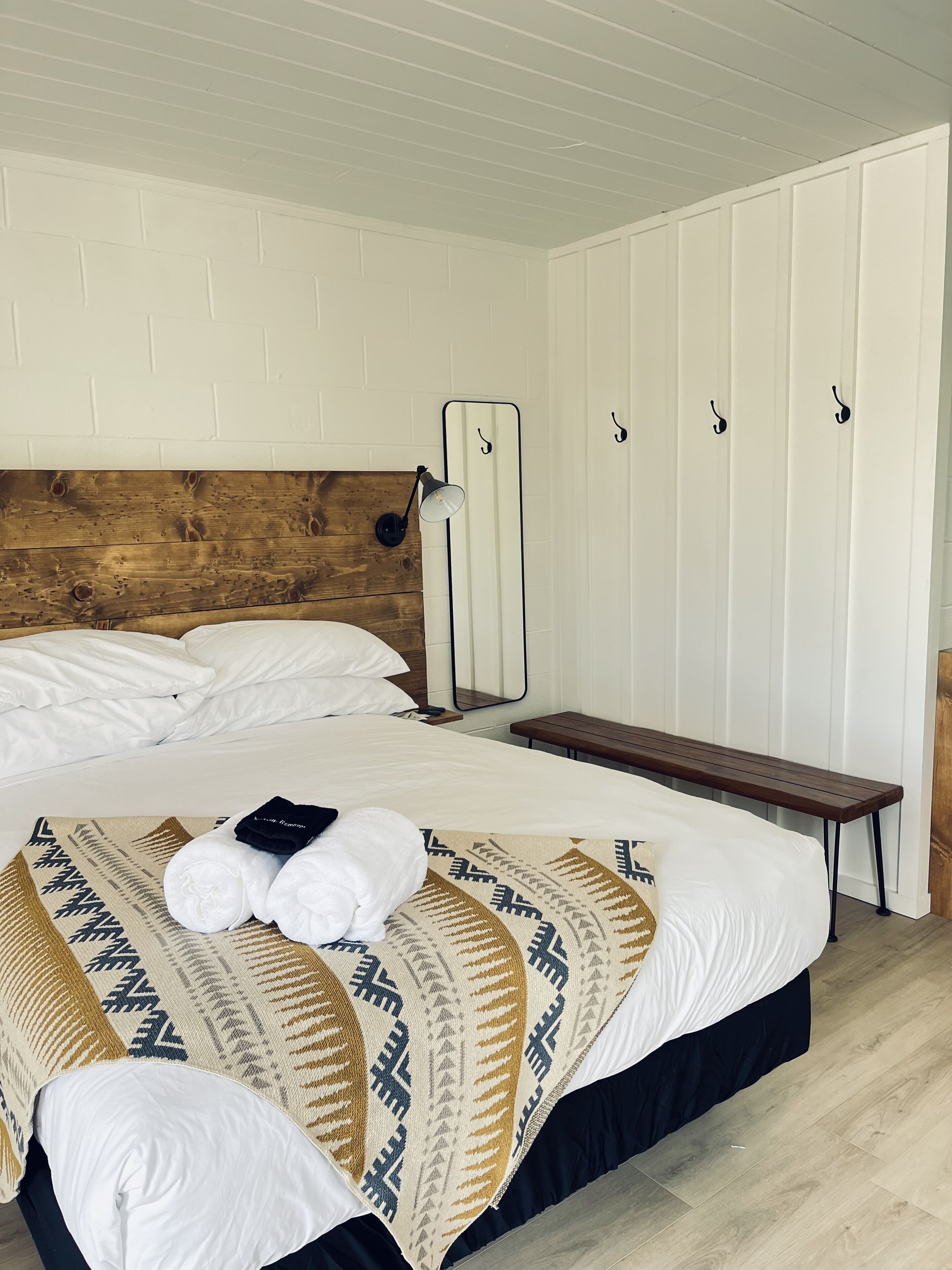 A neatly made bed with a patterned blanket, a wooden headboard, a bedside lamp, and a bench.