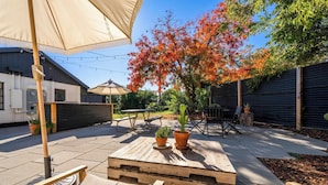 An outdoor patio area with wooden tables and chairs, a pergola with a canopy, and a large tree with autumn foliage. - Triangle Motel (Red Bluff)