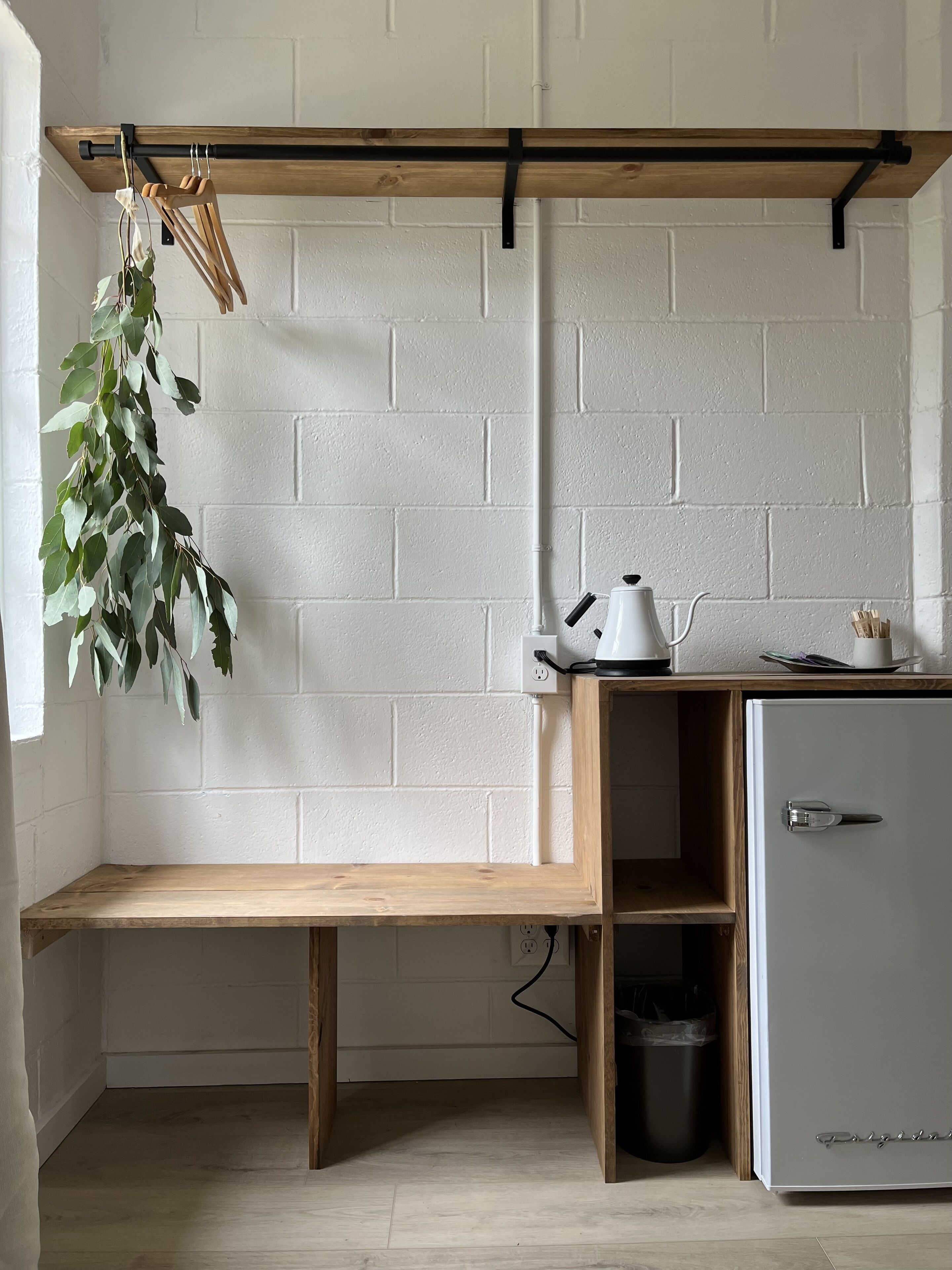 Une petite cuisine équipée avec un banc en bois, un mur en briques blanches et une plante en pot.