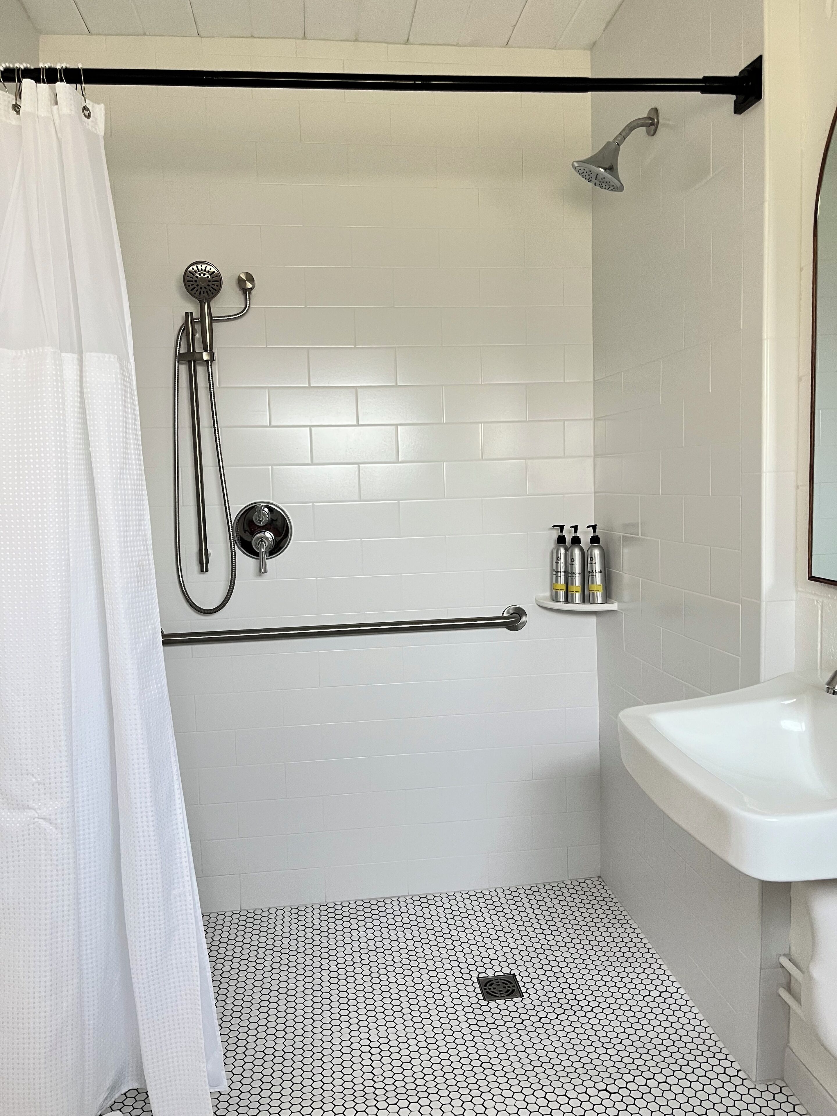 A bathroom with a shower, a toilet, a sink, and a toilet paper holder.