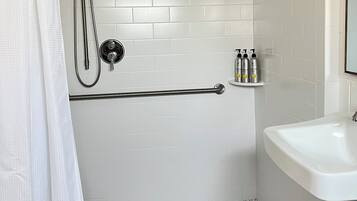 A bathroom with a shower, a toilet, a sink, and a toilet paper holder.