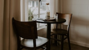 A room with a window, two wooden chairs, a small table, and a framed picture on the wall. - Triangle Motel (Red Bluff)