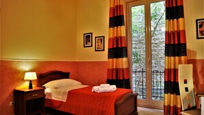 Una habitación de hotel con cama, mesita de noche, lámpara y ventana con cortinas.