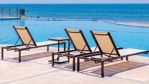 Un espace aménagé au bord de la piscine, avec des chaises longues et une vue sur l’océan.