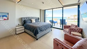 Une chambre moderne avec un grand lit, une table de chevet, un coin salon avec des fauteuils et un balcon offrant une vue sur l’océan.