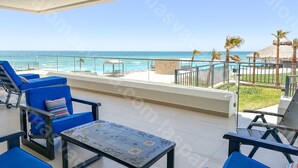 Un balcon avec des chaises bleues et une table, donnant sur une piscine et l’océan.