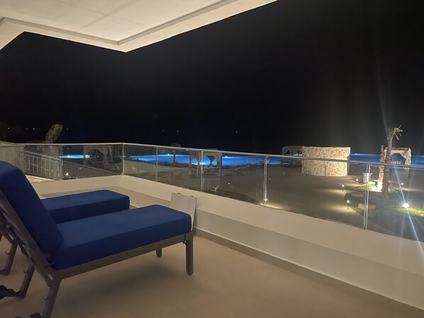 Un balcon avec des fauteuils de jardin bleus, un mur en pierre et une piscine éclairée la nuit.