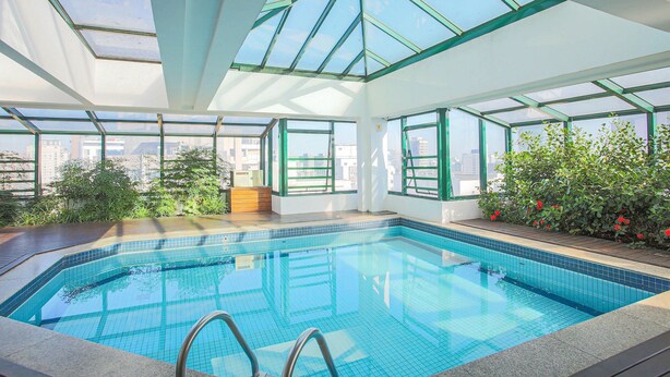 A swimming pool with a glass ceiling, surrounded by greenery and city views. - Edifício Expert (São Paulo)