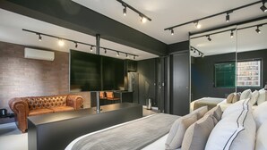 A modern hotel room with a large bed, a sofa, a kitchen area, and a large window. - Edifício Expert (São Paulo)