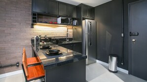 A modern kitchen with dark cabinetry, a stainless steel refrigerator, and a microwave. - Edifício Expert (São Paulo)