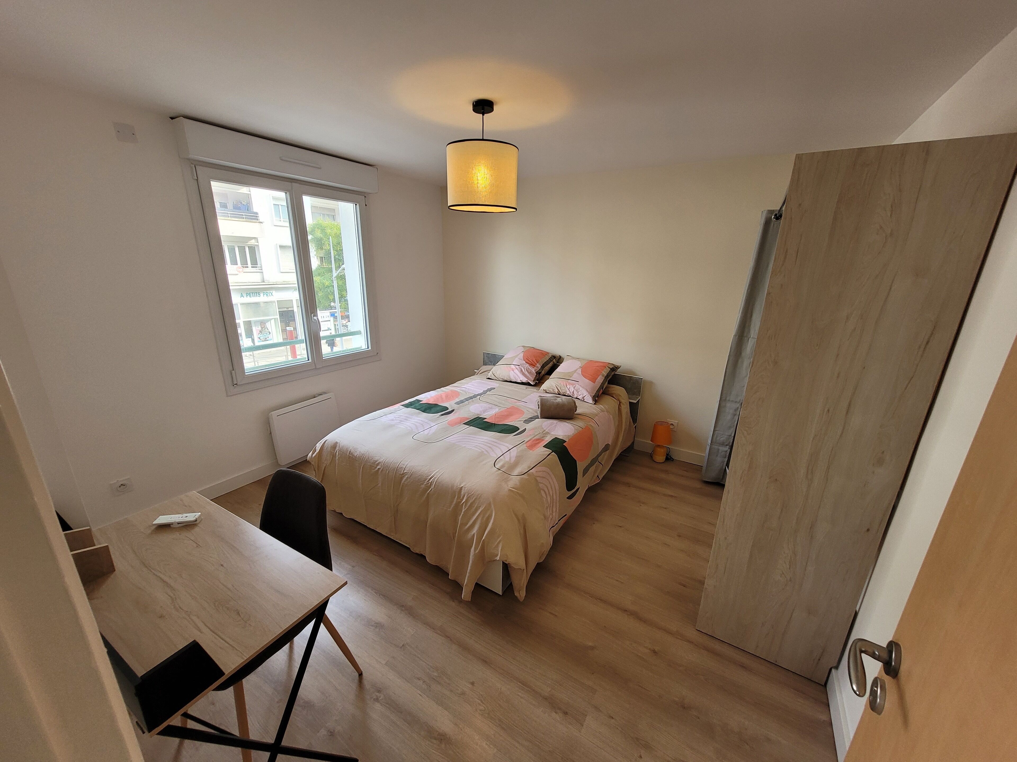 A bedroom with a bed, a desk, a chair, a window, and a door.