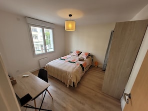 Um quarto com uma cama, uma escrivaninha, uma cadeira, uma janela e uma porta.