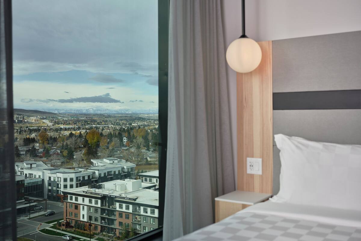 A hotel room with a large window offering a view of a cityscape, including buildings and mountains.