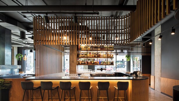 Un espace bar agrémenté d’une cloison en bois, de tabourets de bar et de différentes bouteilles exposées sur des étagères.