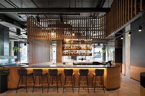 Uma área de bar com divisória de madeira, banquetas e diversos frascos em prateleiras.