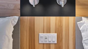 A hotel room with a wooden panel wall, two wall-mounted lamps, a power outlet, and a small wooden table with a notebook and pen.