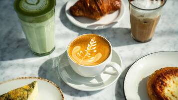 Une table avec une tasse de café, un croissant, un verre de café glacé et une part de gâteau.