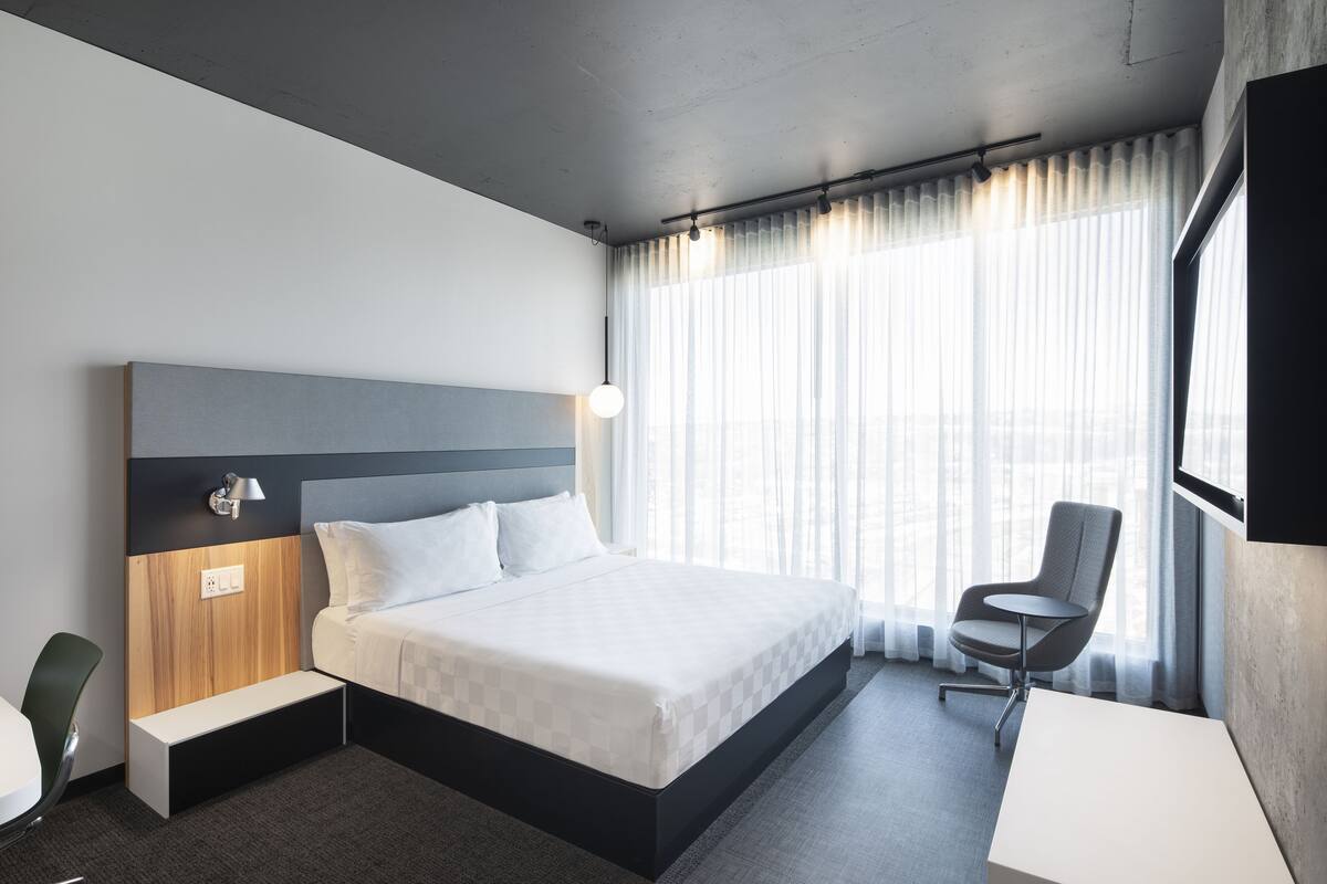 A modern hotel room with a large bed, a desk, and a chair.