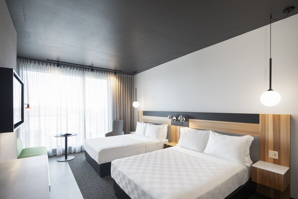 A hotel room with two beds, a small table, a chair, and a TV.