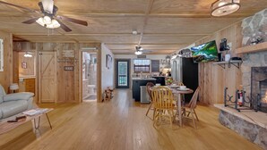 Un vaste espace de vie doté d’un plafond en bois, d’une cheminée, d’une table à manger avec des chaises, et d’une cuisine à l’arrière-plan.