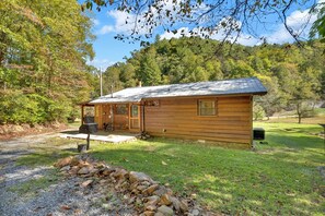 A wooden cabin with a porch, a grill, and a stone wall in front.