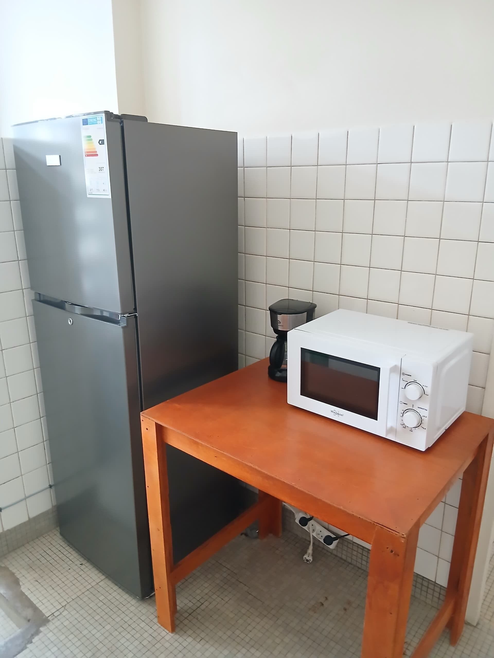 A compact kitchen with a black refrigerator, a white microwave on a wooden table, and a tiled backsplash.