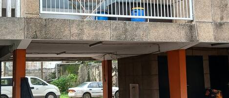 Un edificio de varios pisos con balcones, una zona de estacionamiento techada y un automóvil visible al fondo.