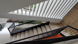 Eine Treppe mit schwarzen Geländern und beigefarbenen Stufen, die zu einem Außenbereich mit Pflanzen und einem gefliesten Boden führt.