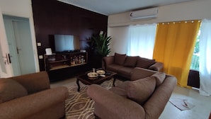 Ein Wohnzimmer mit einer Sofagarnitur, einem Couchtisch, einem Fernseher und einer Pflanze.