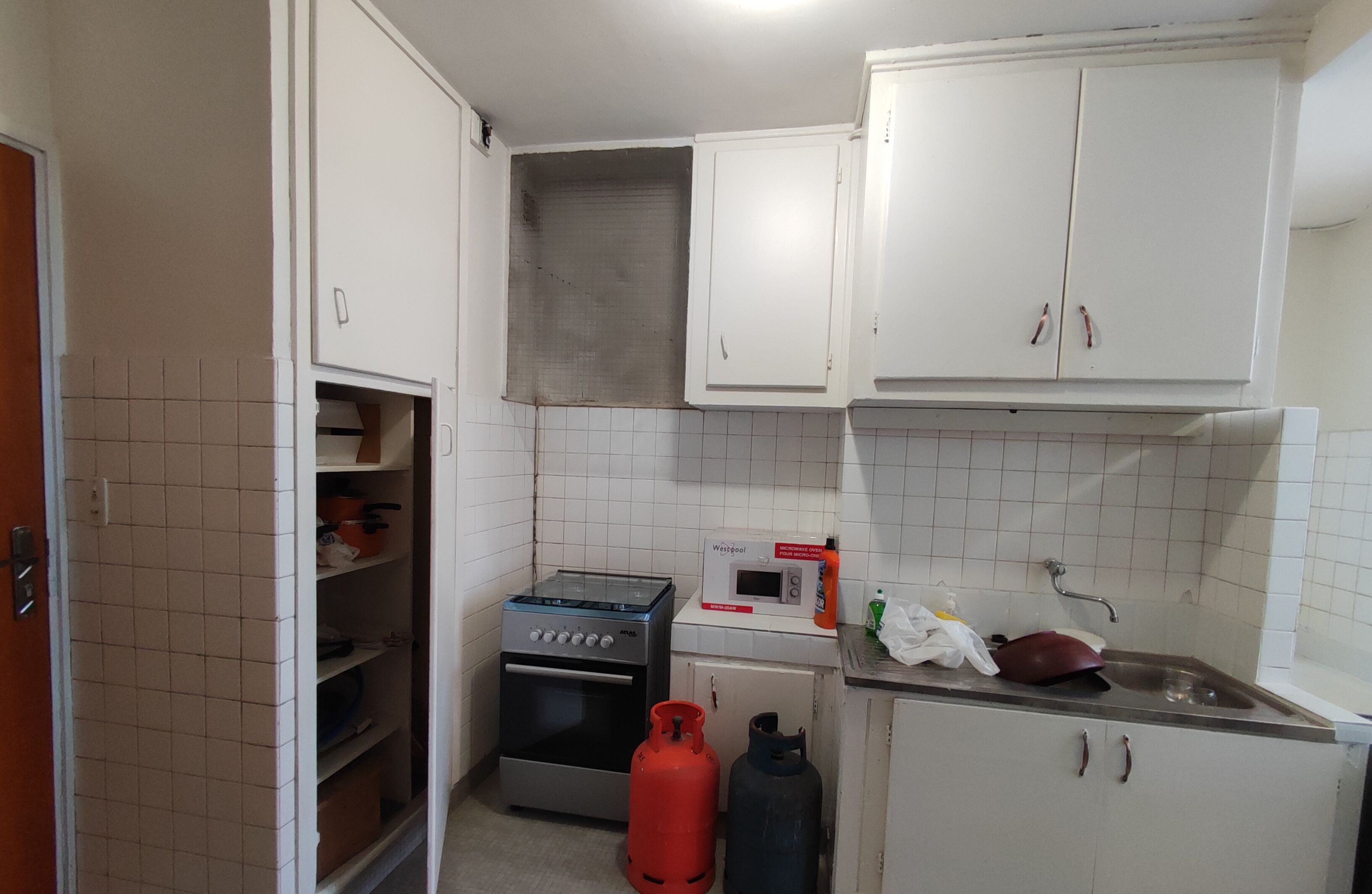 Una cocina compacta con armarios blancos, cocina a gas, microondas y fregadero.