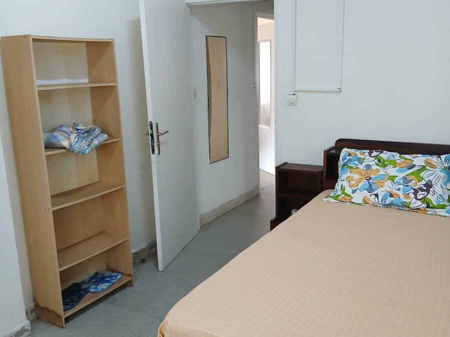 A bedroom with a bed, a wooden wardrobe, and a door leading to another room.