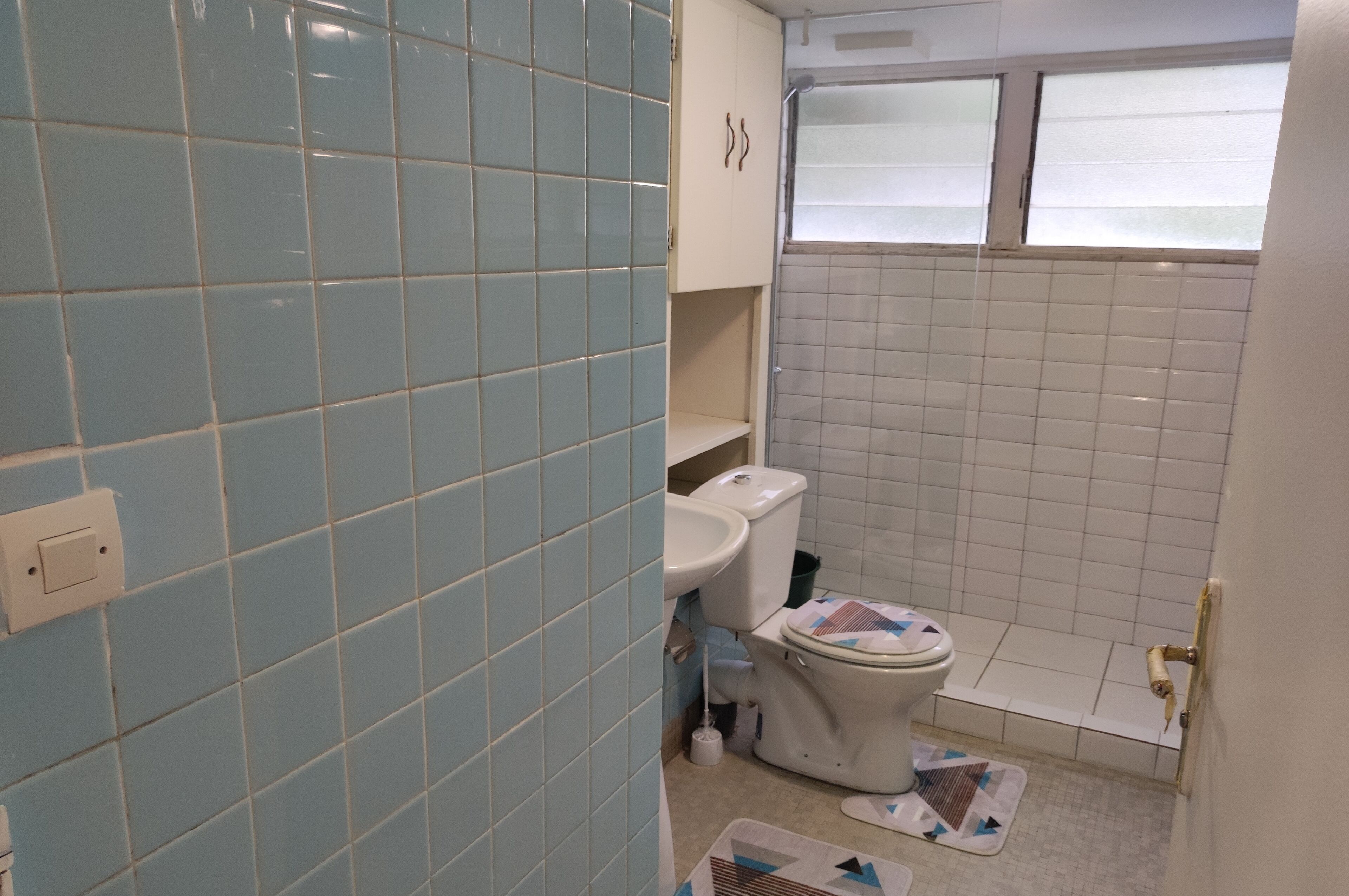 A bathroom with light blue and white tiles, a toilet, a sink, and a window.