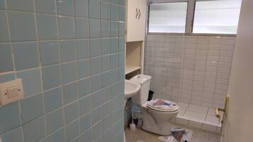 A bathroom with light blue and white tiles, a toilet, a sink, and a window.