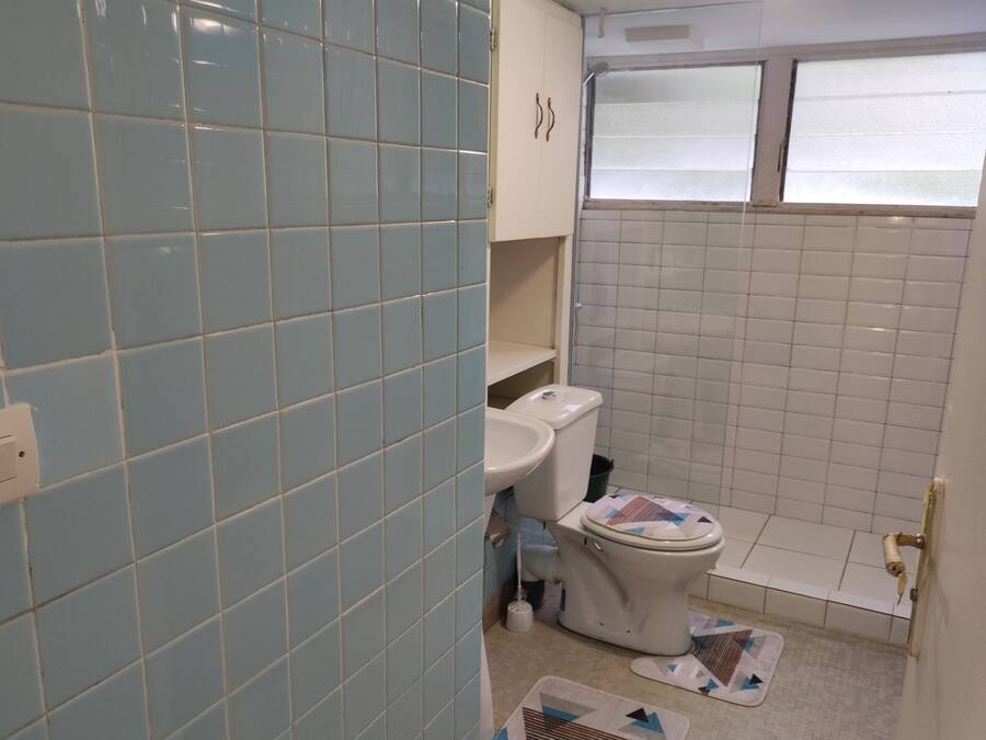 A bathroom with light blue and white tiles, a toilet, a sink, and a window.