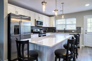 Une cuisine moderne dotée d’un grand îlot central, d’appareils électroménagers en acier inoxydable et de luminaires suspendus.