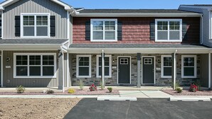 A two-story residential building with a garage on the left, a covered porch in the center, and a second garage on the right. - New Condo! Minutes from Sand Springs Golf Course & Wedding/Event Venue (Drums)