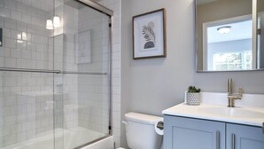 A modern bathroom with a glass shower enclosure, a toilet, and a sink with a mirror above. - New Condo! Minutes from Sand Springs Golf Course & Wedding/Event Venue (Drums)
