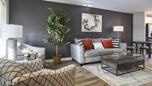 A modern living room with a grey sofa, a glass coffee table, and a large plant. - New Condo! Minutes from Sand Springs Golf Course & Wedding/Event Venue (Drums)