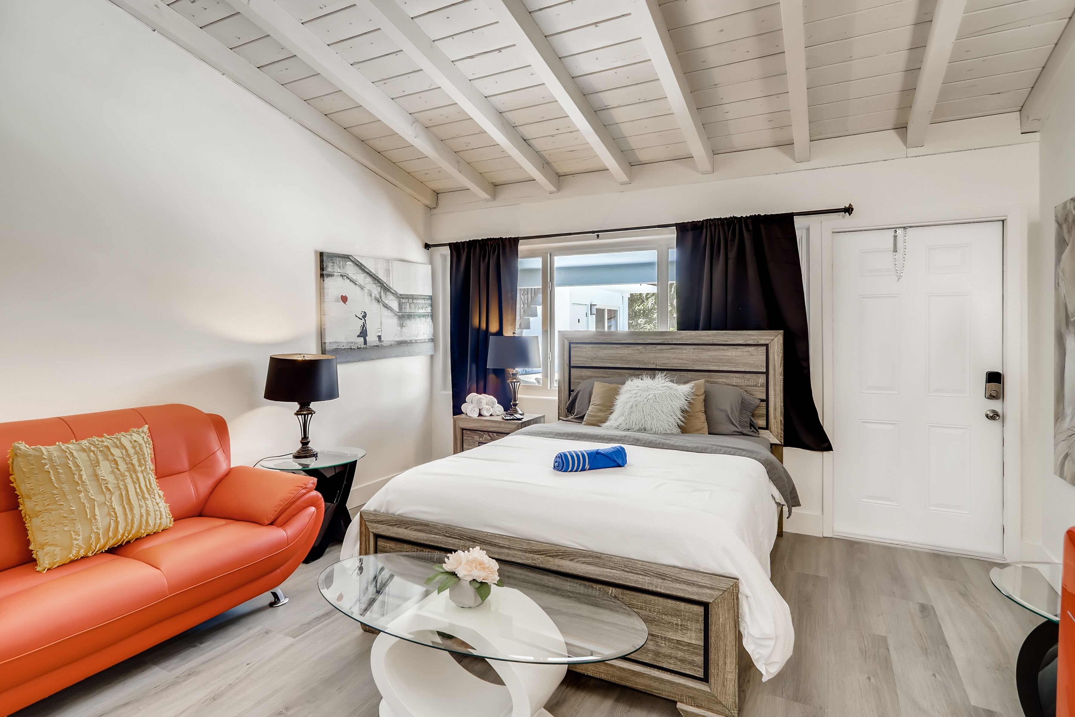 A bedroom with a bed, a glass coffee table, a sofa, and a door.