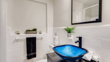 A bathroom with a white tiled wall, a black sink with a blue basin, a white toilet, a black towel, and a small plant on a shelf.