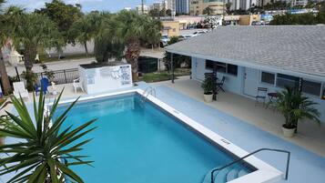 Una piscina con una escalera, rodeada de palmeras y un edificio con terraza.
