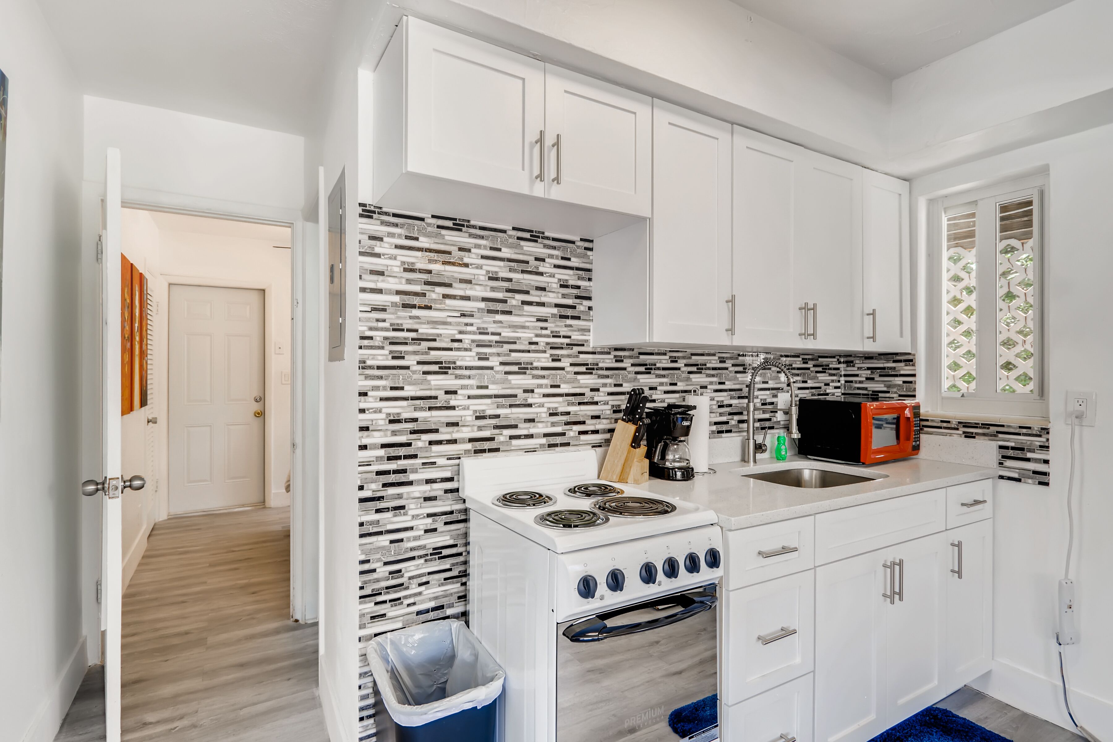 A modern kitchen with white cabinets, a patterned backsplash, a stove, a microwave, and a sink.
