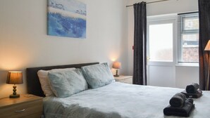 Ein Schlafzimmer mit einem Bett, zwei Nachttischlampen, einem Bild an der Wand und einem Fenster mit Vorhängen.