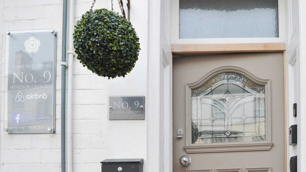 Eine Geb äudefassade mit einem Schild für No. 9 Windsor Crescent, einer Airbnb-Anzeige, einer Tür mit Fensterteil und einer Metallklopfrose.