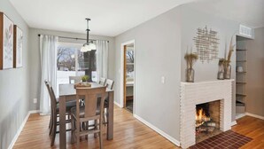 Ein Essbereich mit Holztisch und -stühlen, einer Hängeleuchte und einem Kamin mit Dekoration.