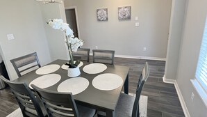 A dining area with a dark wooden table, white placemats, and chairs. There is a vase with white flowers on the table.