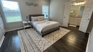 A bedroom with a bed, nightstands, a rug, a ceiling fan, and a bathroom visible through an open door.